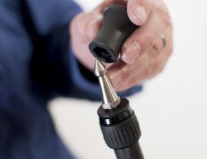 Close-up image of a man in a blue shirt removing the rubberized cover on a Cameron CF tripod foot, revealing the spiked foot underneath