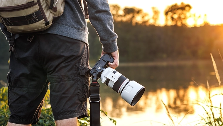 A bird photographer holding a DSLR with a telephoto lens, and wearing a backpack