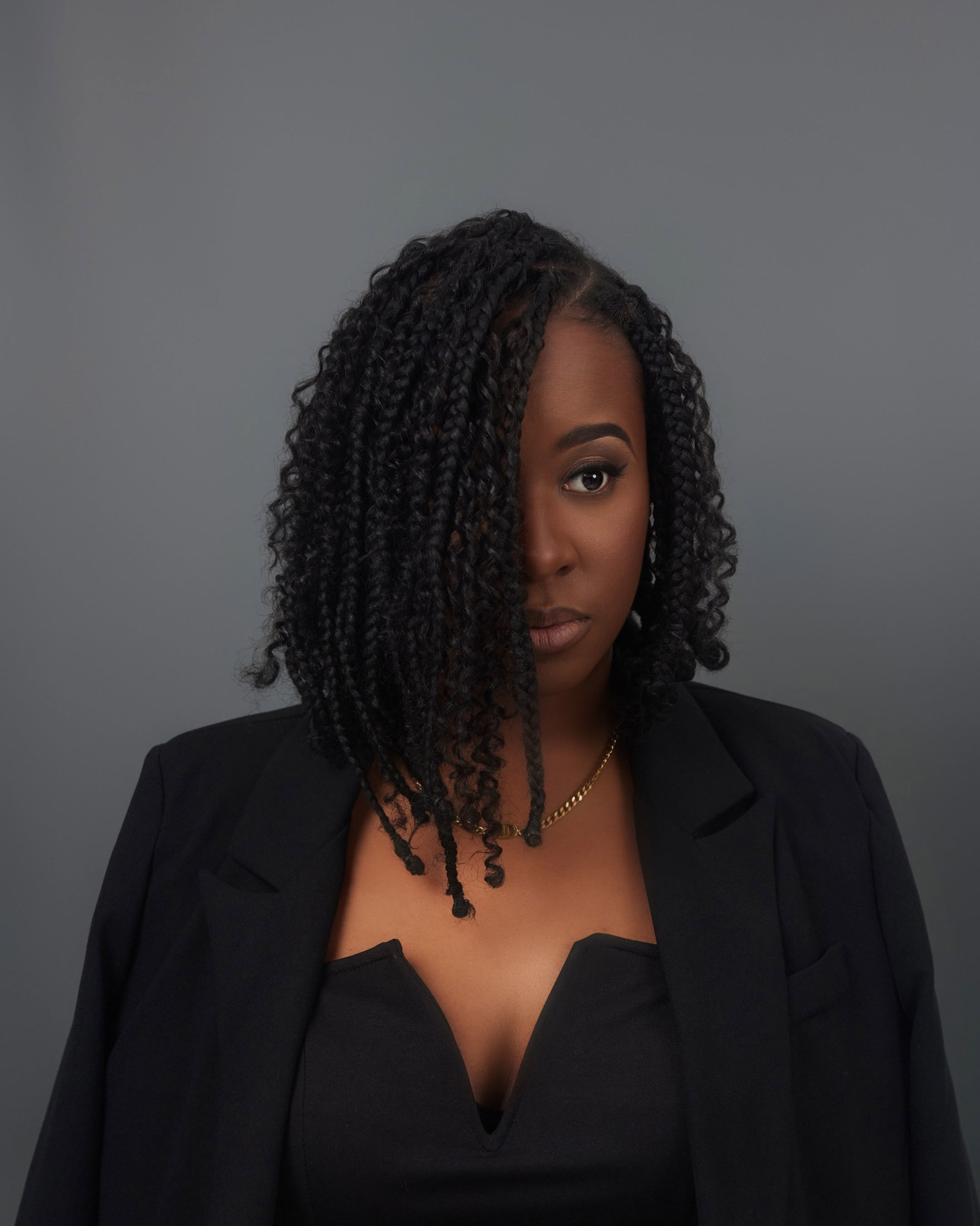 An elegantly dressed young black woman with short braided hair covering part of her face.