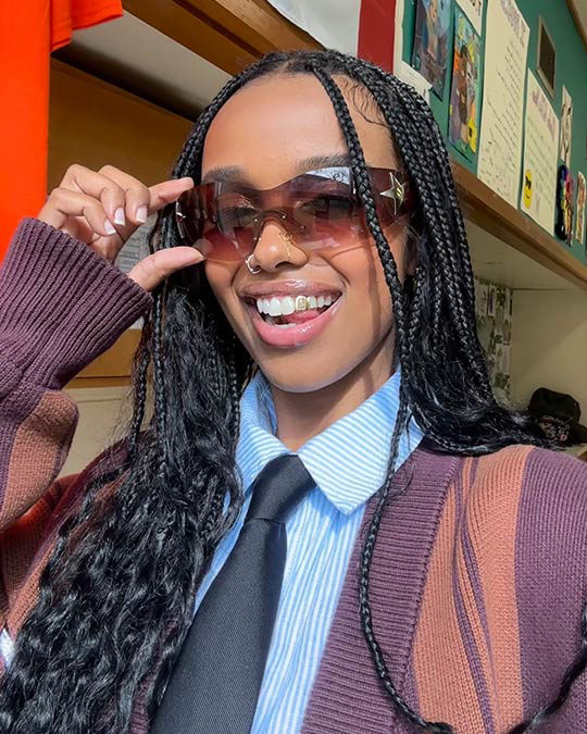 A young black woman wearing stylish sunglasses smiling at the camera