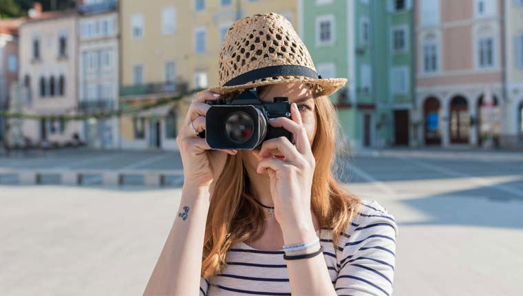 A young woman wearing a hat and taking a photo somewhere in Europe