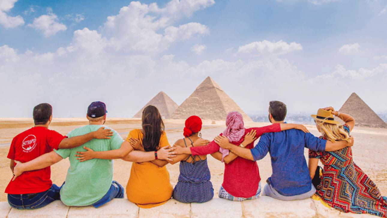 A group of people wearing traditional clothes of various cultures looking at the pyramids of Egypt