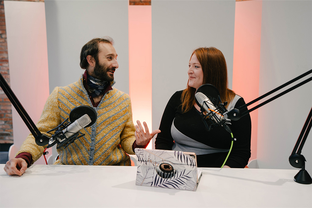 A man and a woman sitting at a table recording a podcast