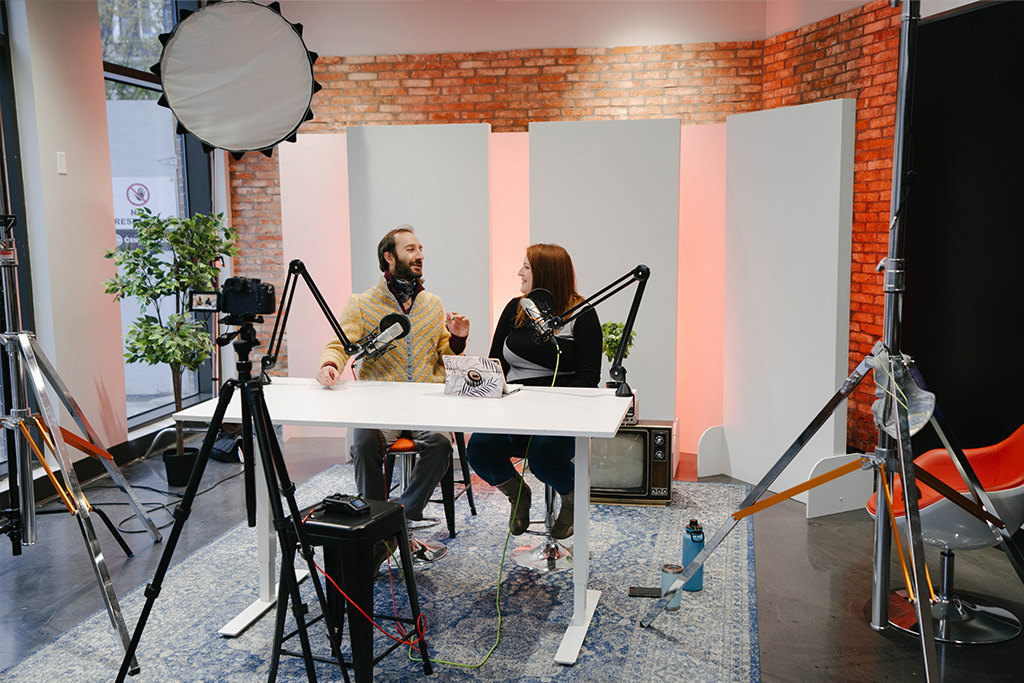 A man and a woman sitting at a table recording a podcast