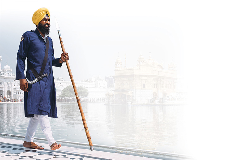 a Sikh walking beside the water in front of a temple
