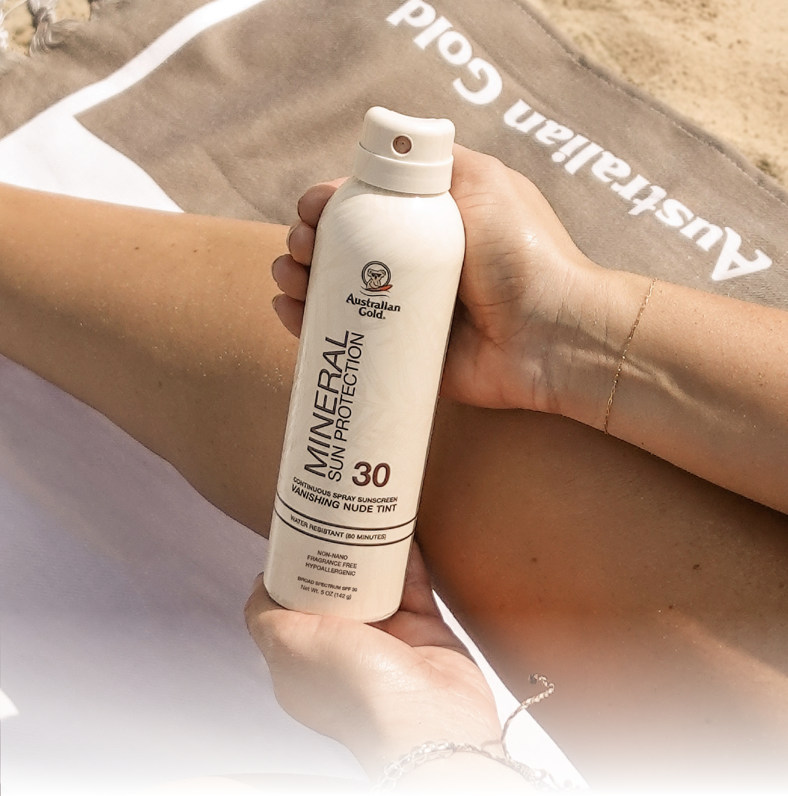 SPF 30 Mineral Continuous Spray held by person on a beach towel