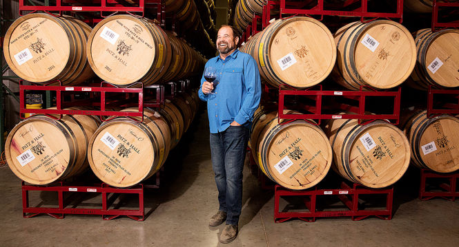 James Hall standing with a glass of red wine in the barrel room