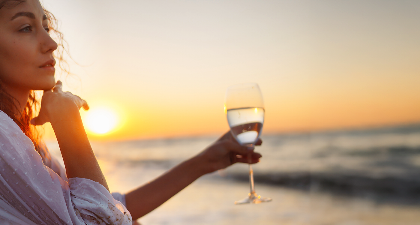 Woman holding up a glass of wine by beach