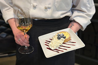 Person holding a dessert and glass of wine
