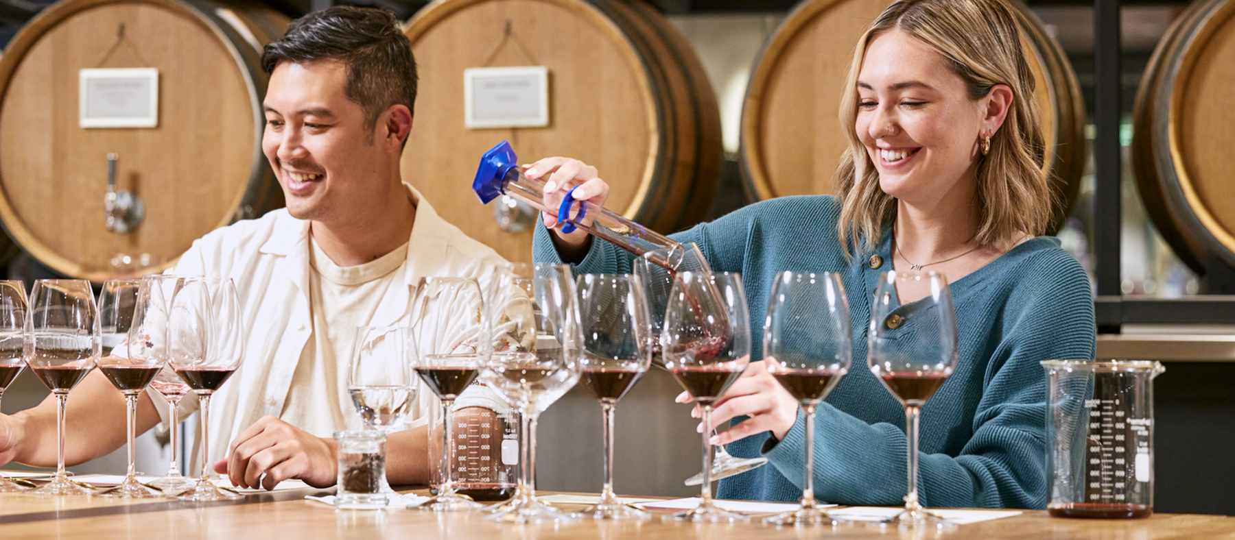 A couple mixing wines with wine barrels in the background