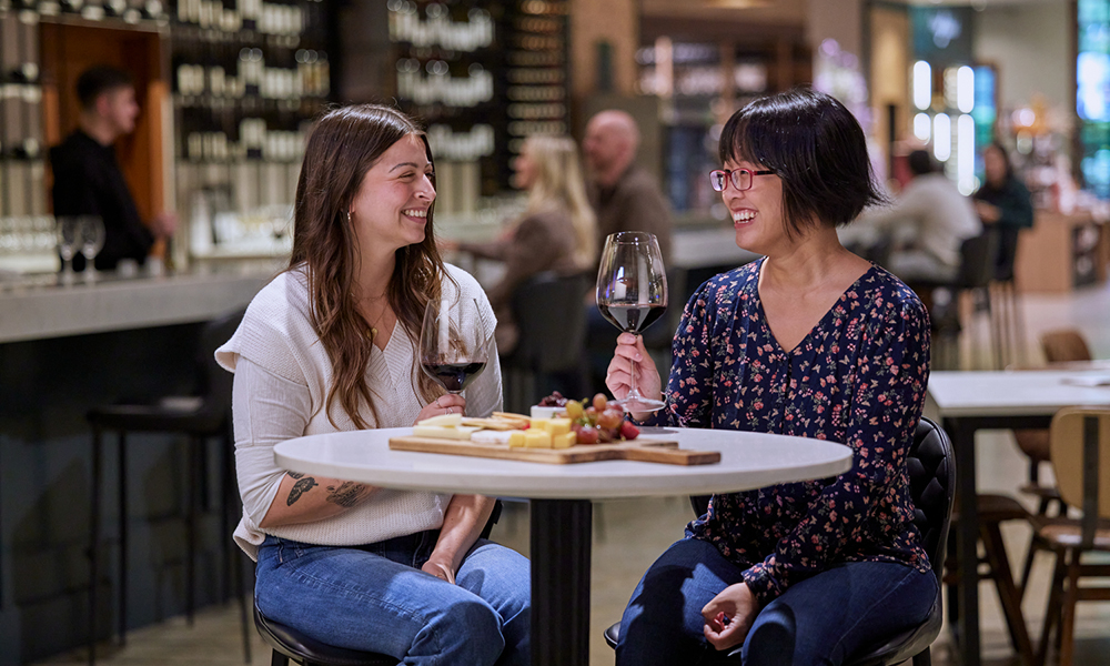  two women drinking red wine at a table in the tasting room