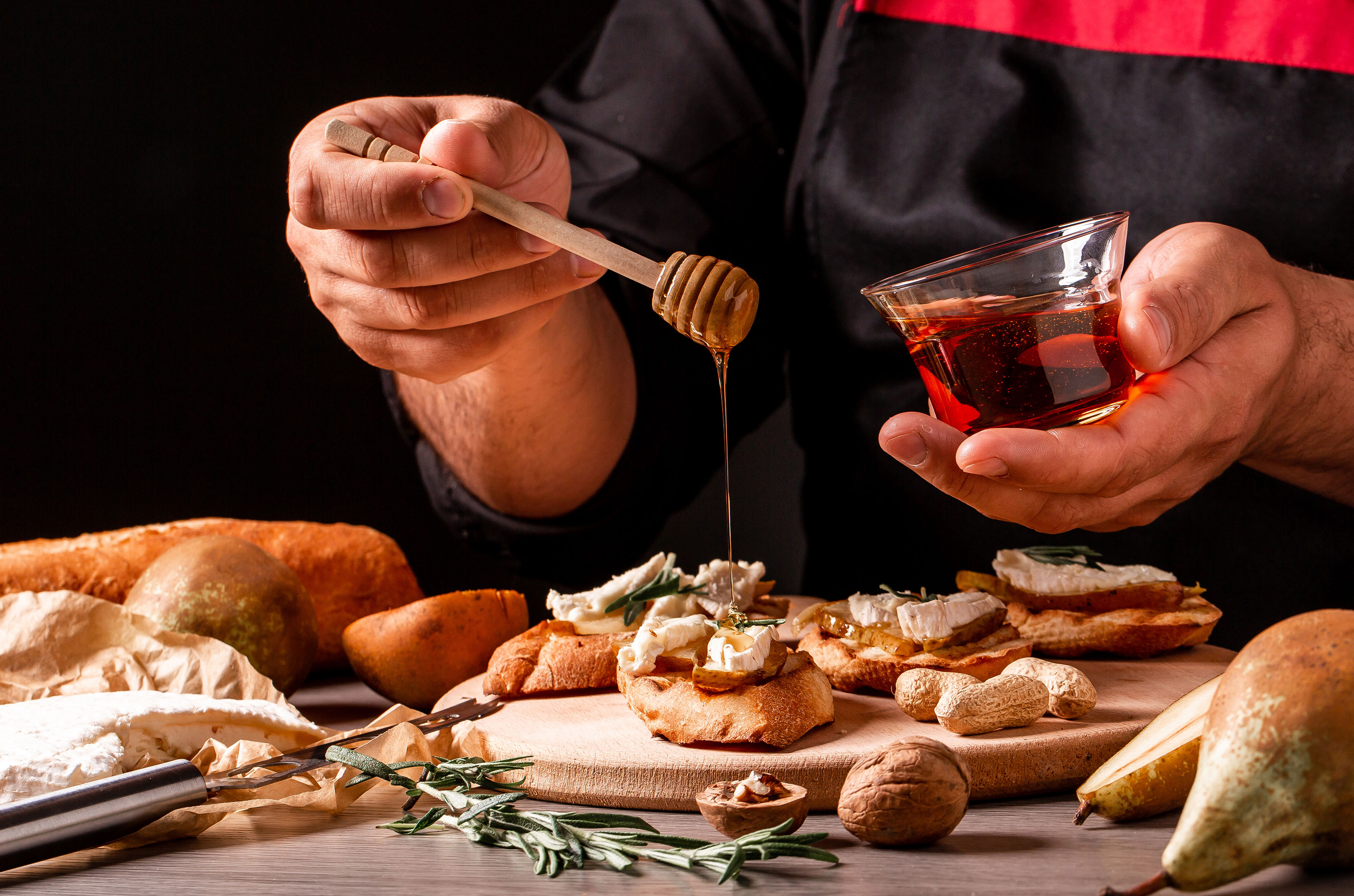 person drizzling honey over goat cheese on a baguette