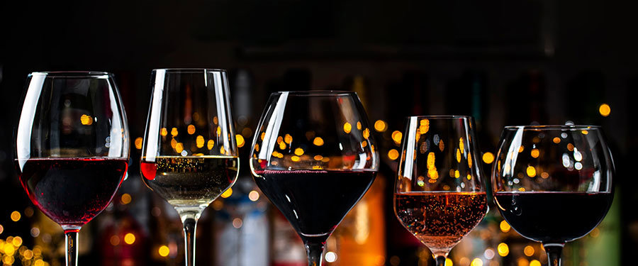 Glasses of wine lined up in front of wine bottles