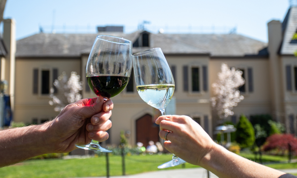 Hands holding up glasses of red and white wine in front of the Chateau