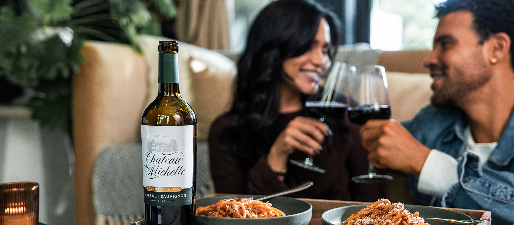 A man and woman eating spaghetti dinner drinking red wine