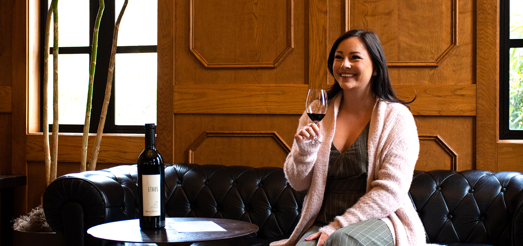 Woman seated on leather couch enjoying a glass of red wine in VRC member room