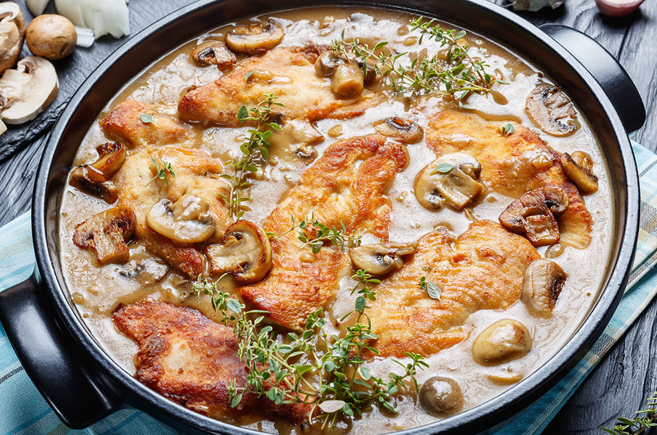 Seared pork chops in a skillet, simmering in a rich Dijon and mushroom cream sauce and topped with fresh herbs