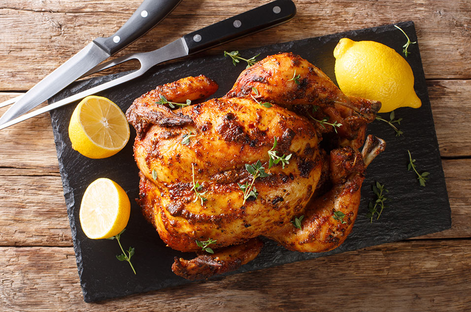A succulent oven roasted chicken on a cutting board, accompanied by fresh lemon wedges, showcasing its golden-brown, crispy skin and juicy interior
