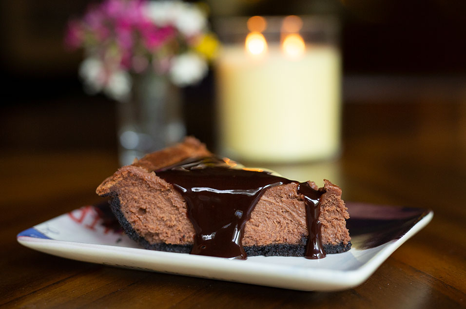 Chocolate cheesecake on a table in front of a candle and flowers