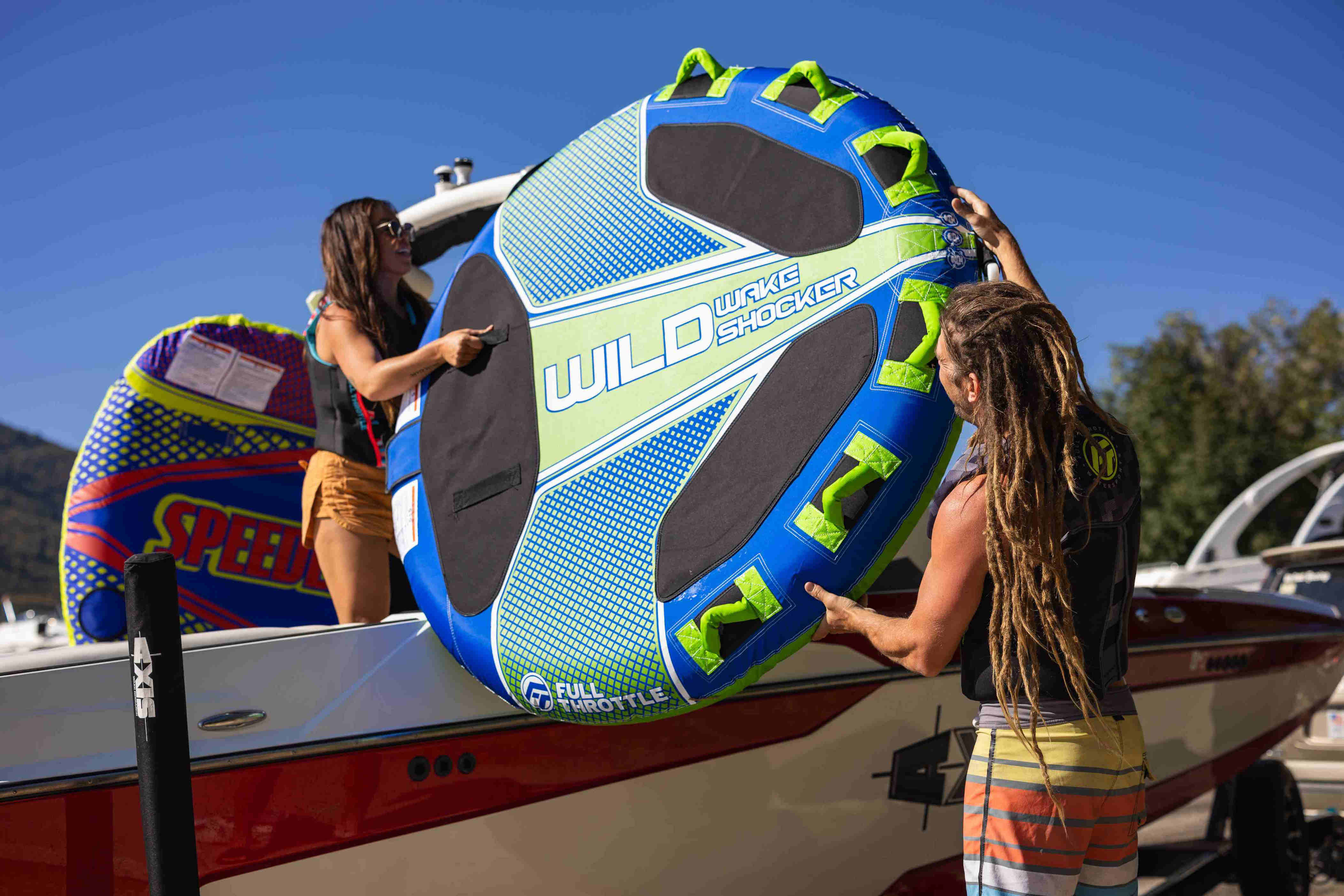 Two people load a towable tube onto a boat.