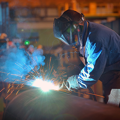 A factory scene featuring a man engaged in welding steel pipes, demonstrating craftsmanship and industrial activity