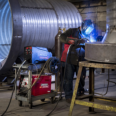 Un homme soude des tuyaux industriels dans une usine à l'aide d'équipements Lincoln Electric