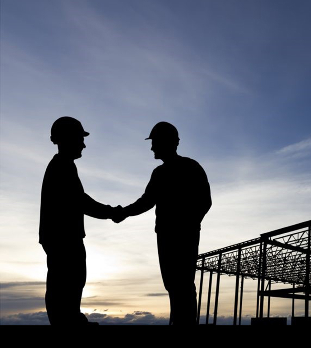 Silhouette of two contructions workers shaking hands in agreement on a contruction site