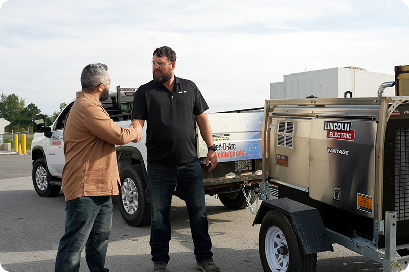 Client et employé se serrant la main devant le camion de l'entreprise lors d'une livraison de matériel de soudage