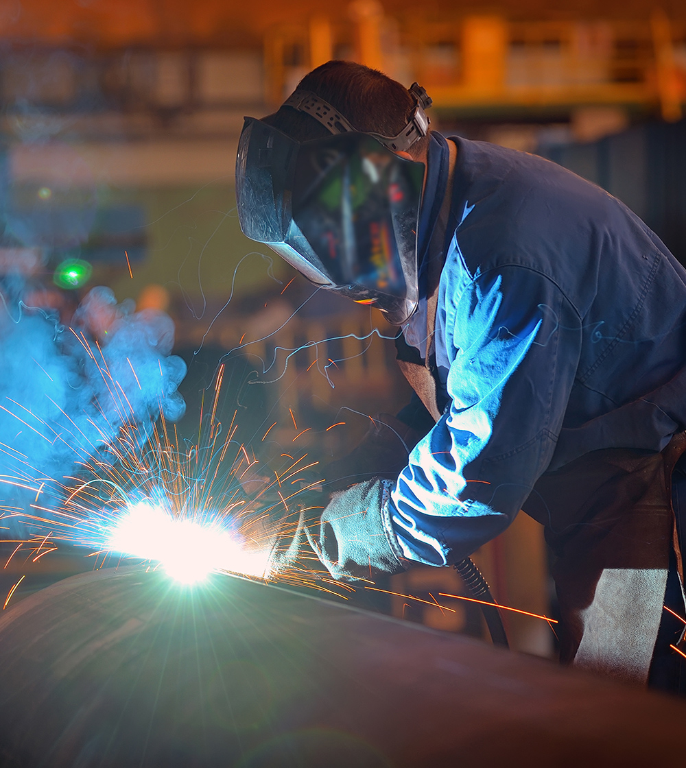 Worker performing MIG welding on an industrial pipe inside a shop