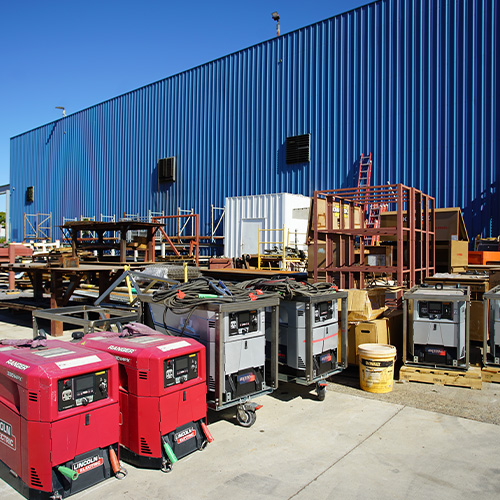 A variety of used welders lined up outside of a warehouse