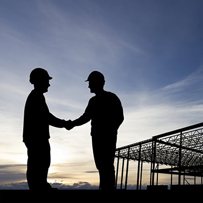 Silhouettes of two men engaged in a handshake on a construction site, representing partnership and mutual understanding in a business context