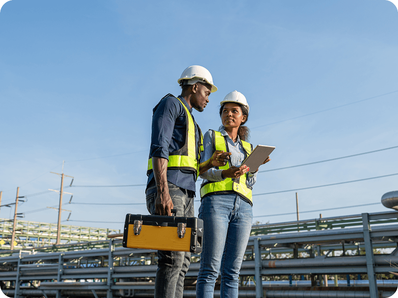 a man and a woman in hard hats looking over a notepad on a construction site