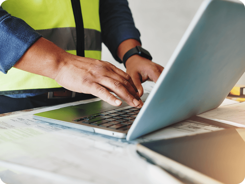 a man in a safety vest on a job site using a laptop
