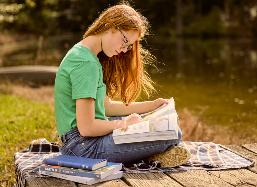 a teen girl sitting outside reading her textbooks