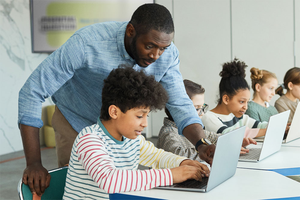 a teacher helping students with laptops